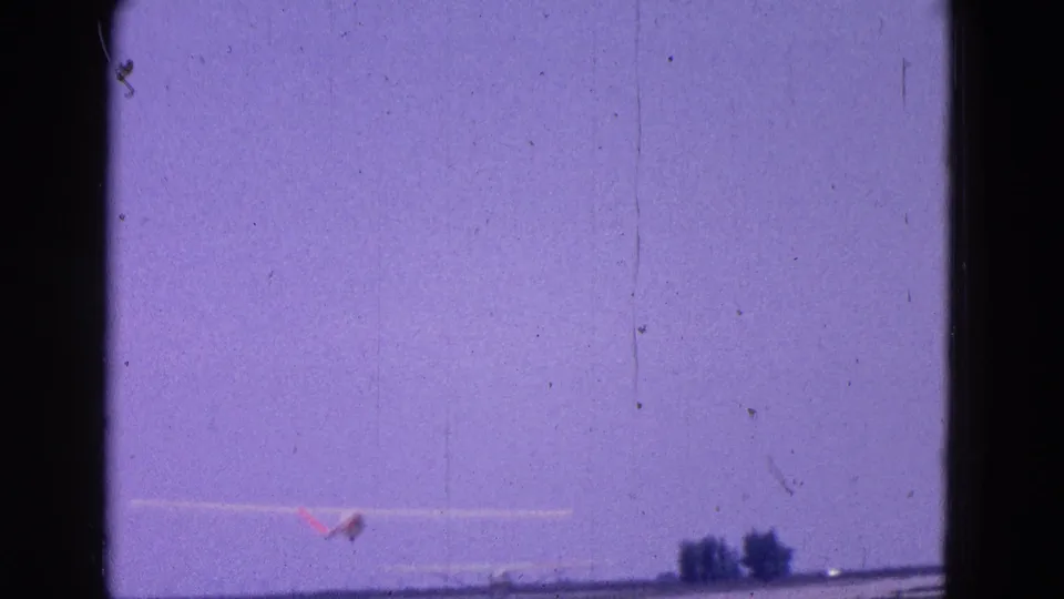 The experimental aircraft appears airborne in the distance above the runway landscape under a purple-shifted sky.