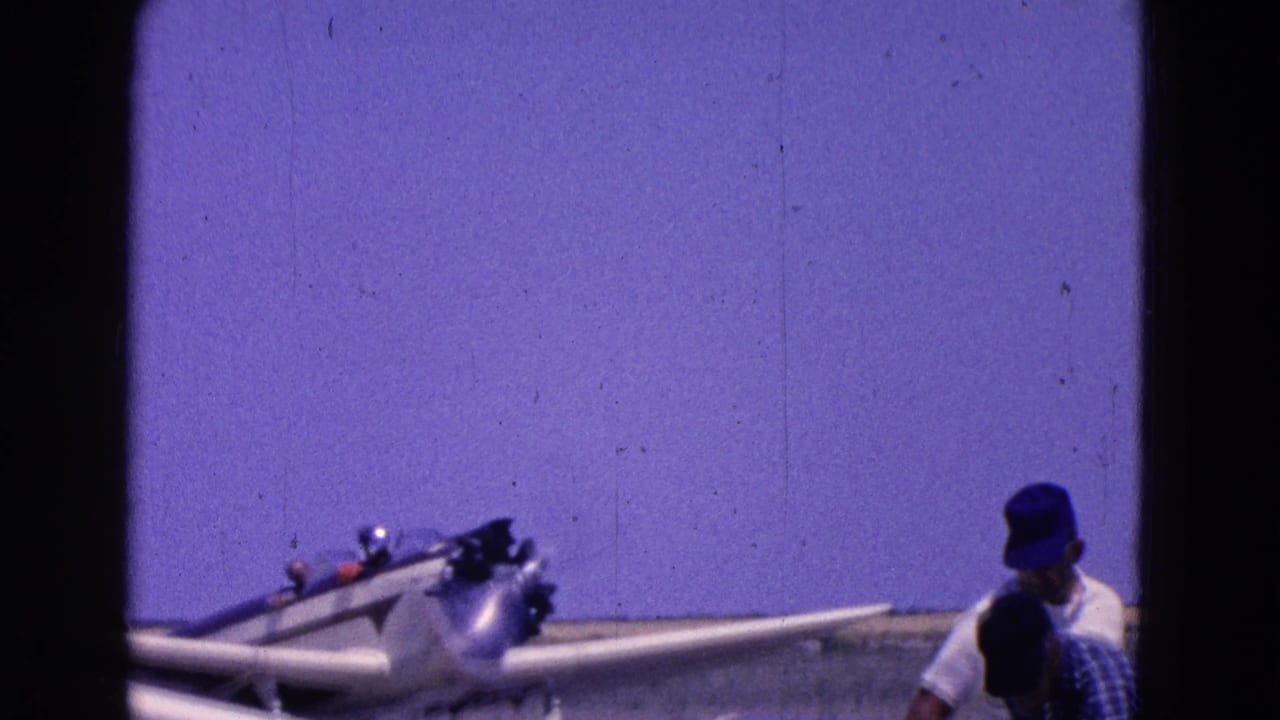 Small propeller aircraft near a man in a blue cap on an open field.