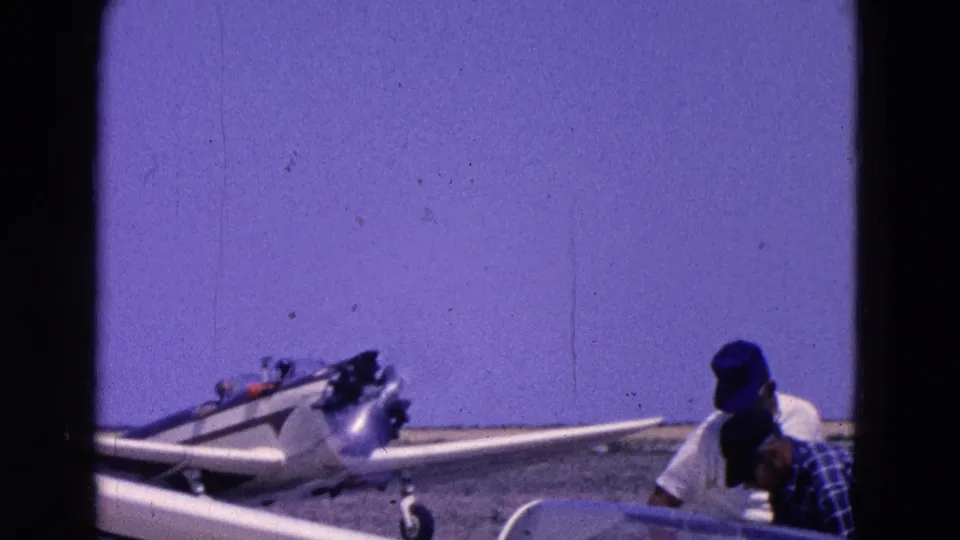 Two people appear near a small aircraft, one in a blue cap and one in plaid, in Washington, DC area home-movie footage from 1964.