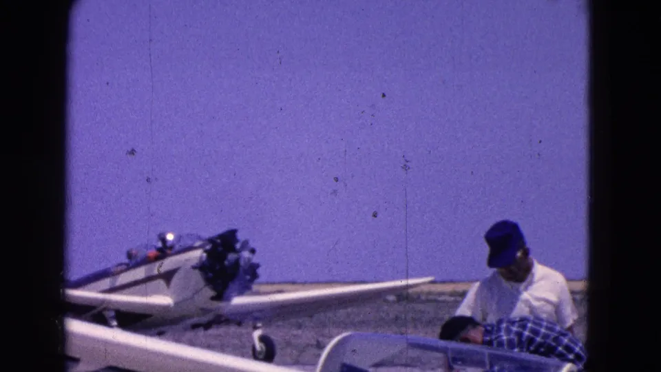 A small aircraft rests on open ground while two people stand or bend nearby in 1964 8mm footage from the Washington, DC area.