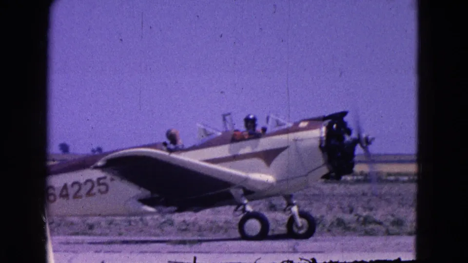 The small white and brown aircraft marked 64225 is seen from the side on a flat airfield under clear sky.