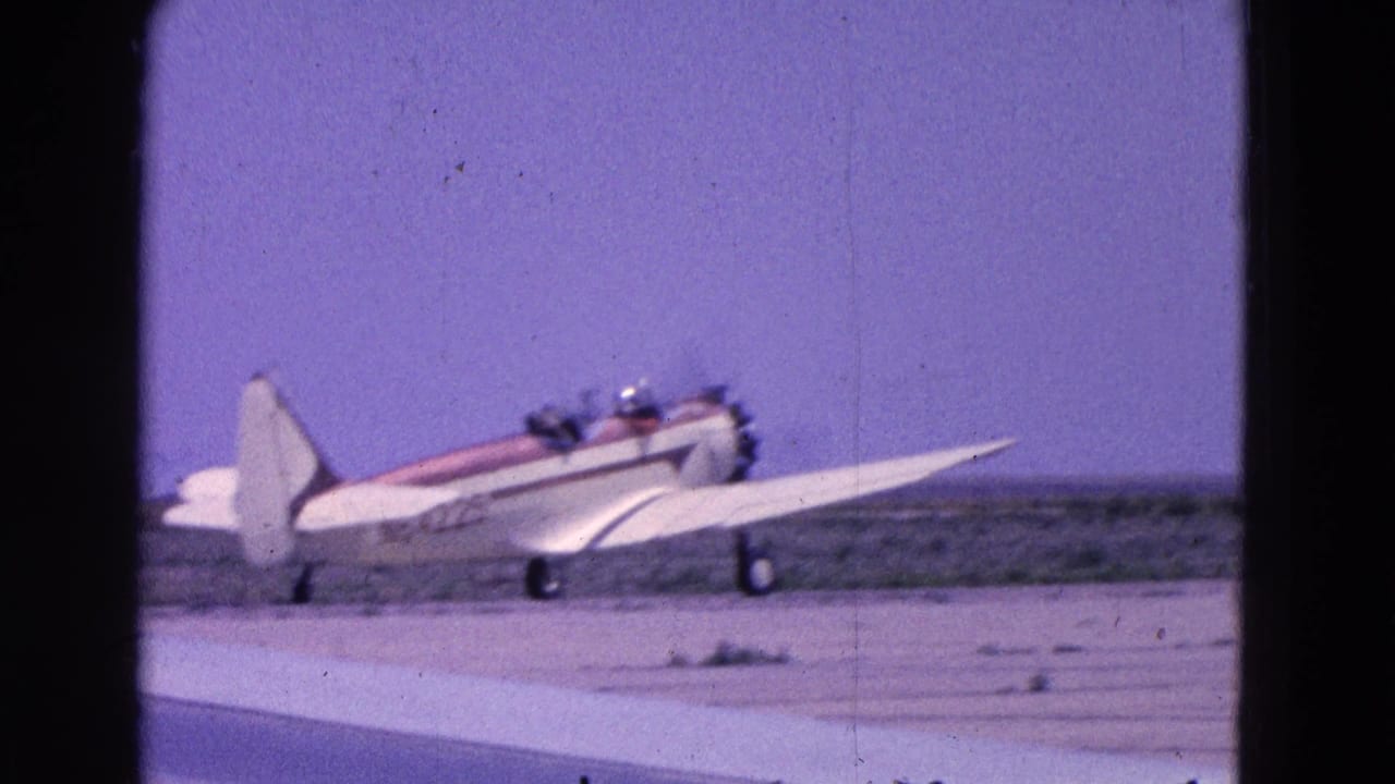 Small propeller plane on a runway, seen side-on with cockpit occupants visible.