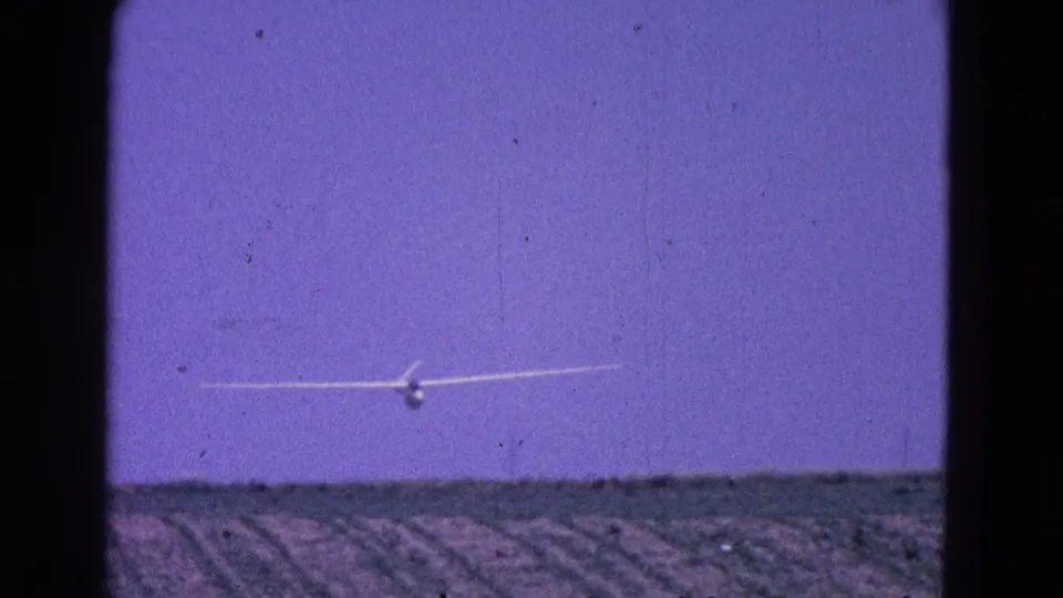 White glider with long wings approaches over rural fields in 1964 Washington DC home-movie footage.