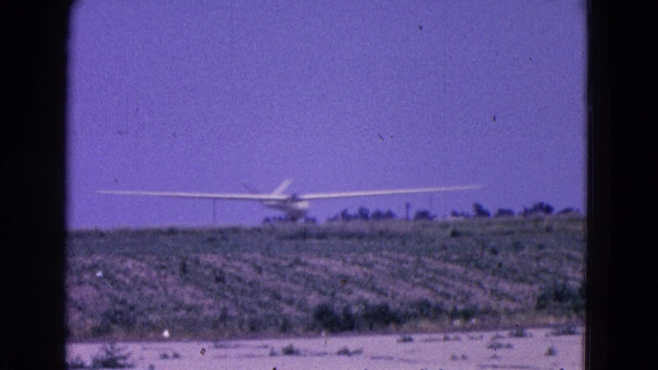 Distant white glider approaching over a rural field beneath a purple sky.