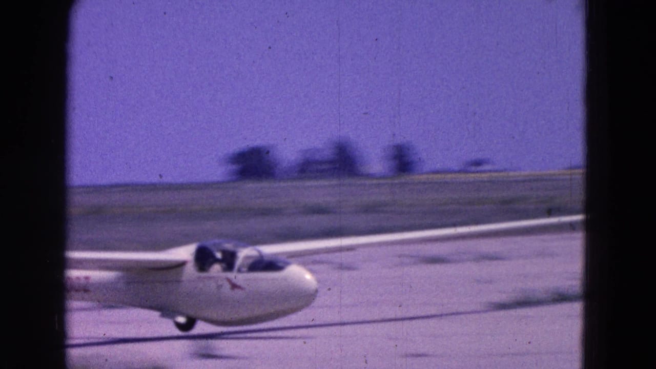 White glider taxiing on a runway with pilot visible in the cockpit.
