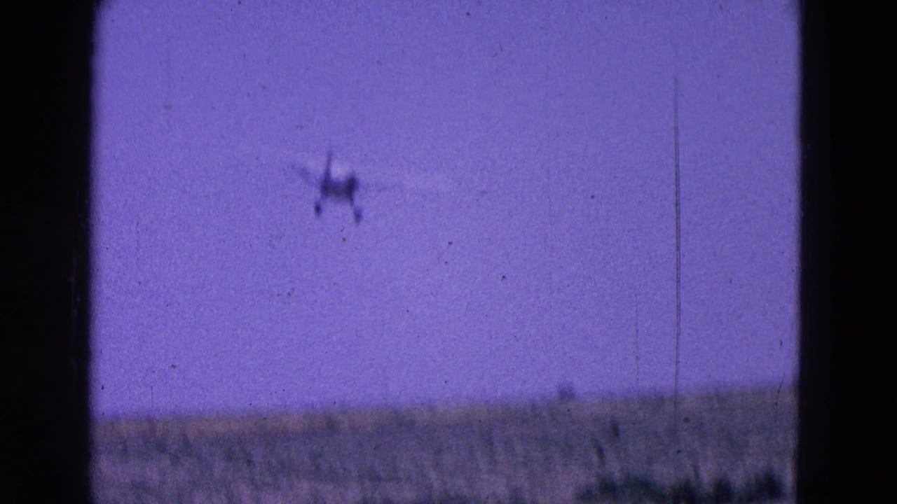 1964 8mm frame from the Washington, DC area showing a small aircraft high over a faint horizon and open blue sky.