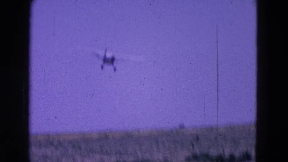 1964 8mm frame from the Washington, DC area showing a small aircraft high over a faint horizon and open blue sky.