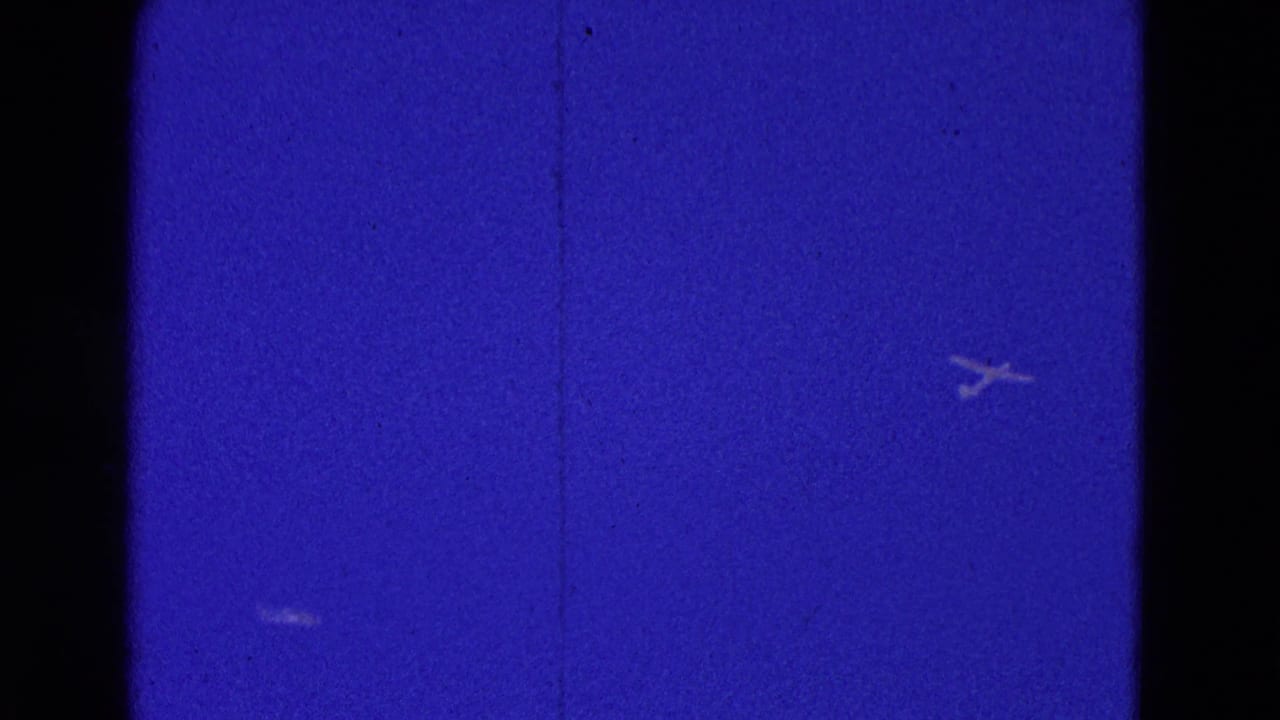 Two distant aircraft shapes appear in a deep blue sky with film borders.