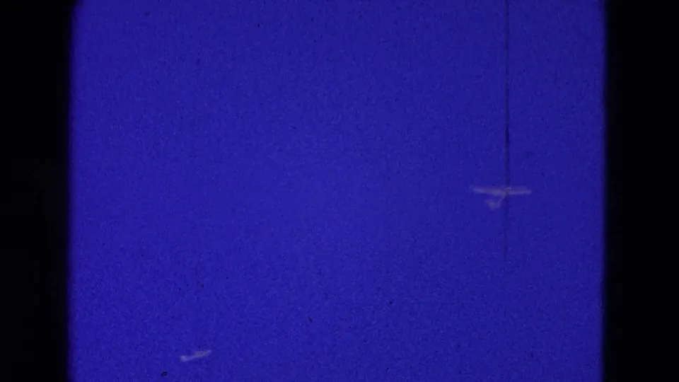 A small aircraft shape appears low in the 8mm frame against blue sky, with visible border, grain, and color shift.