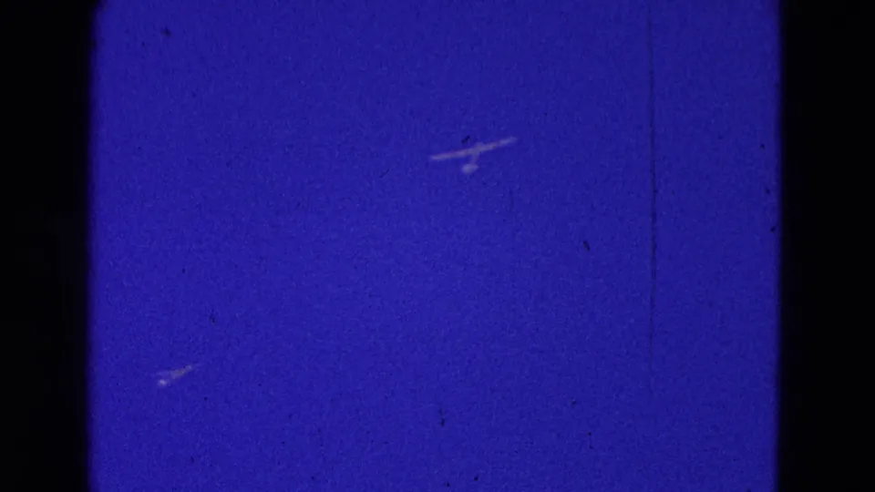The 1964 Washington, DC 8mm frame shows multiple distant aircraft shapes scattered across a blue sky with gate edges and grain.