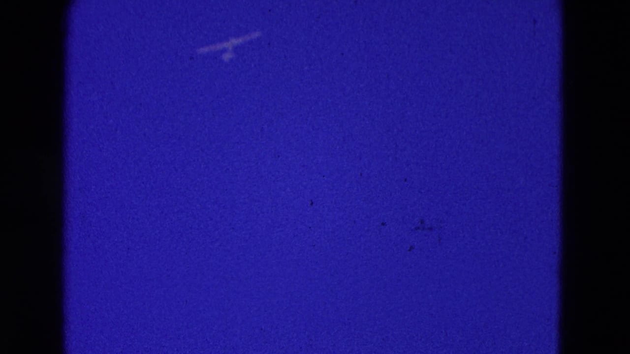 Small pale aircraft shape against a deep blue sky with dark film borders.
