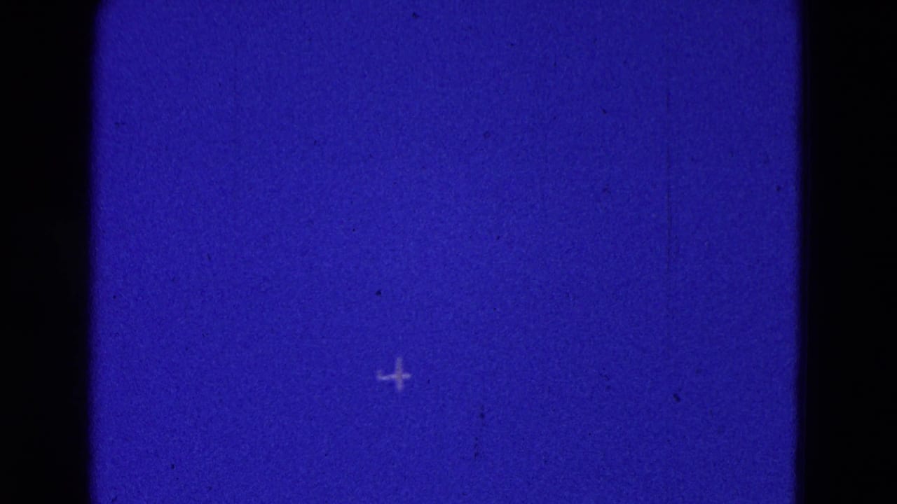 Tiny aircraft silhouette in blue sky beside a dark vertical film divider.