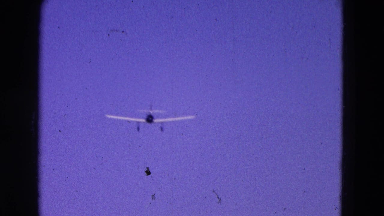 1964 Washington DC 8mm frame of a small white plane approaching through blue sky with landing gear visible.