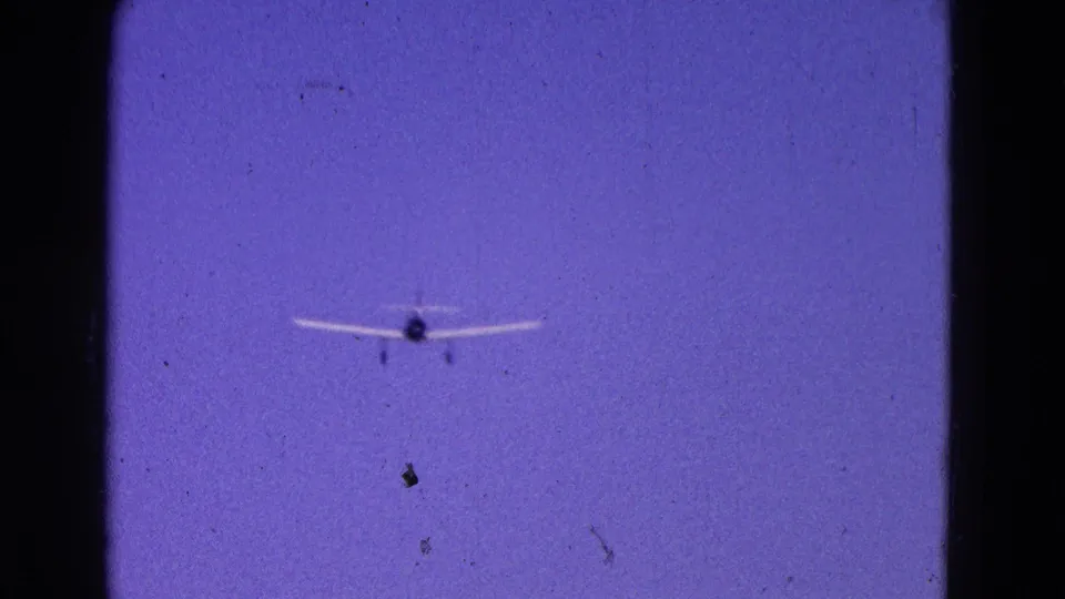 1964 Washington DC 8mm frame of a small white plane approaching through blue sky with landing gear visible.