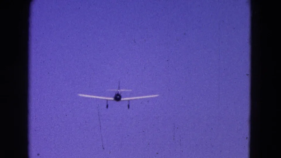 1964 Washington DC 8mm frame showing a small plane approaching from below center against a saturated blue sky.