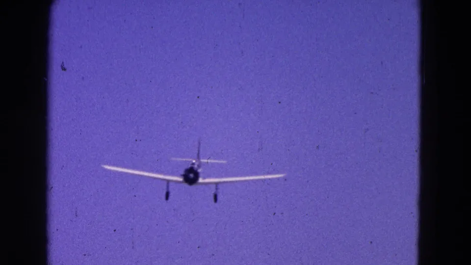 1964 Washington DC 8mm frame of a small white aircraft closer to camera, landing gear down against open blue sky.