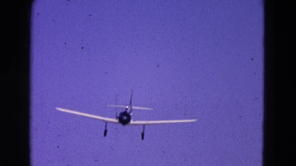 1964 Washington, DC 8mm frame showing a small propeller airplane approaching head-on against a purple-blue sky.