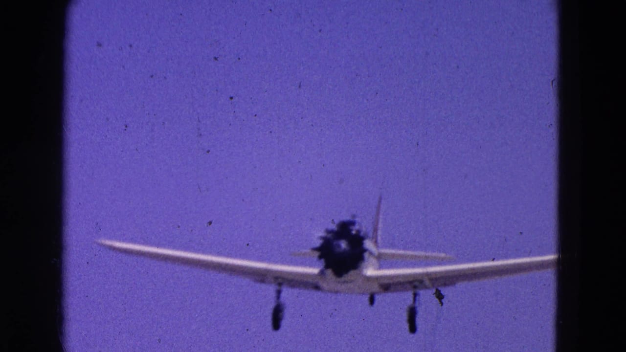 Small propeller airplane nearing the camera in a 1964 Washington, DC home-movie frame, with landing gear extended.