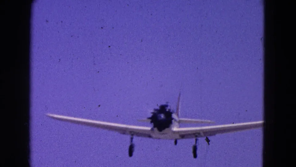 Small propeller airplane nearing the camera in a 1964 Washington, DC home-movie frame, with landing gear extended.