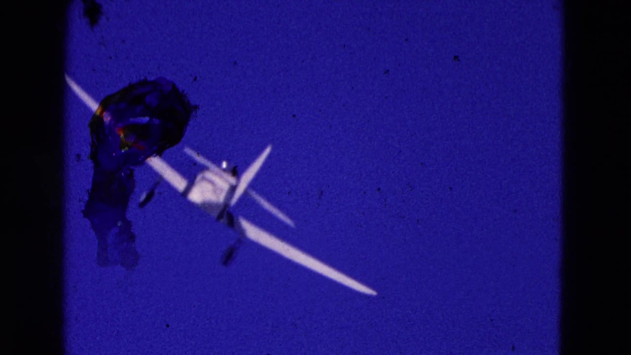 The small white aircraft recedes across the blue sky, framed by dark 8mm gate edges and visible film debris.