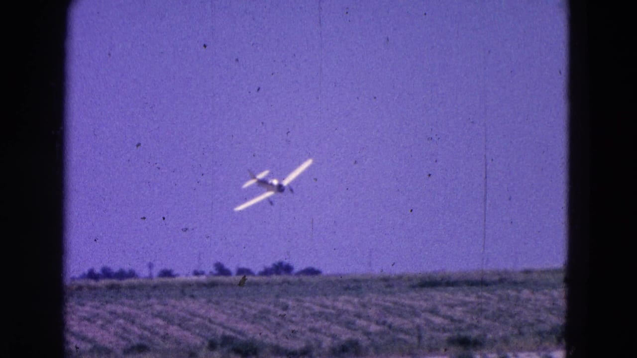 Small propeller plane flying low over an open field beneath a purple-blue sky.