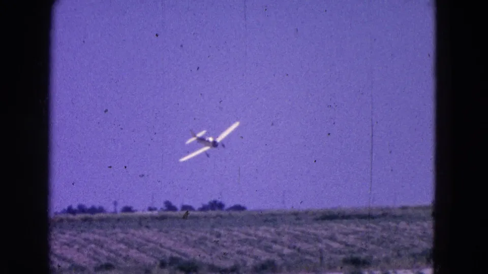 1964 8mm frame of a small propeller plane approaching low over open land in the Washington, DC metadata context.