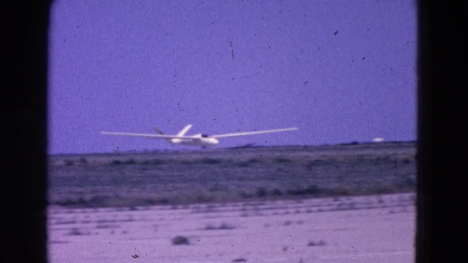 1964 8mm frame from the Washington, DC area showing the small white propeller plane just airborne over low scrubland.