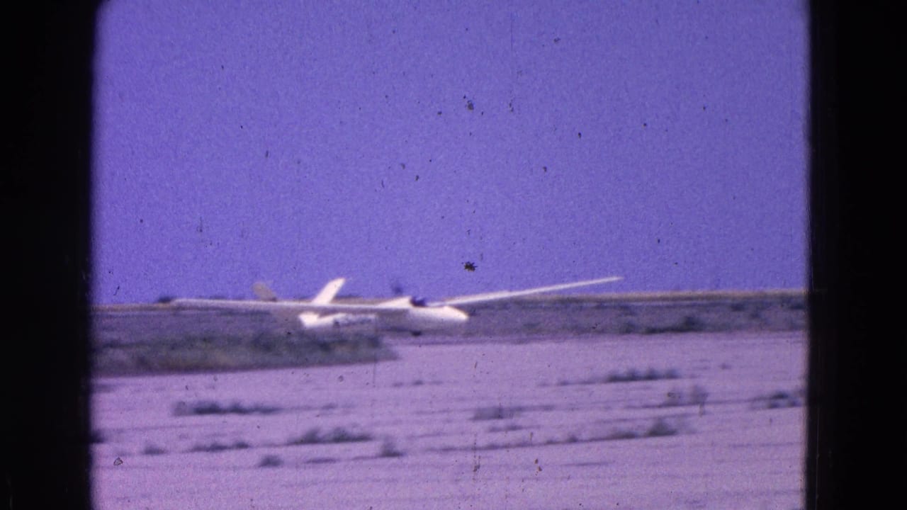 White glider rolling or touching down on a pale open airfield.