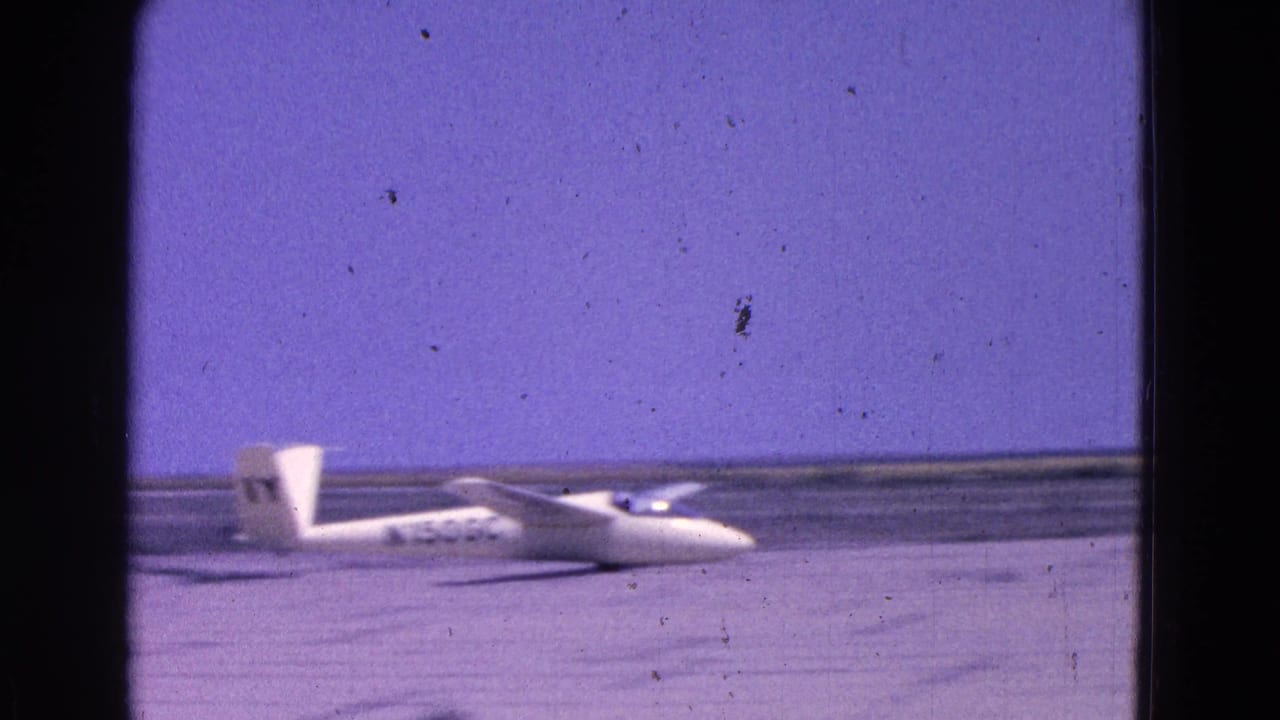 The glider appears to move along the runway in the 1964 home-movie footage, with its nose low and tail markings visible.
