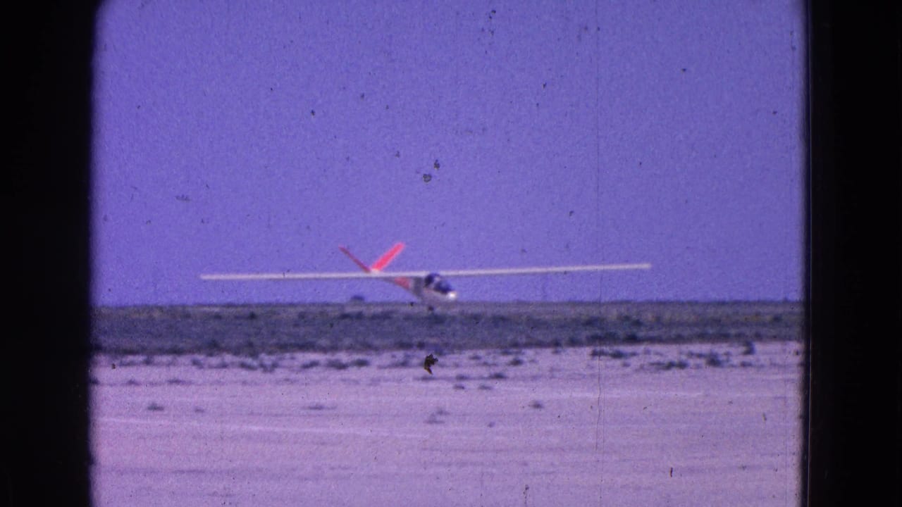Glider nearing the ground on a dusty runway with its wings nearly level.