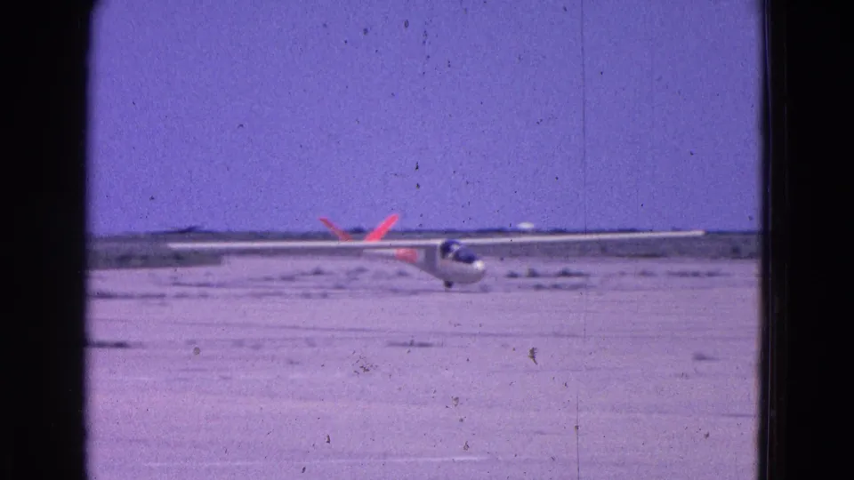 The white glider sits or rolls on the Washington DC-area airstrip, its red tail markings visible under a purple-tinted 8mm sky.
