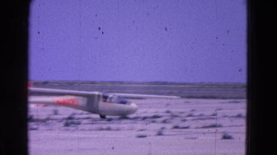 Close 1964 home-movie view of the white glider rolling on the runway, with pilots faintly visible under the canopy.