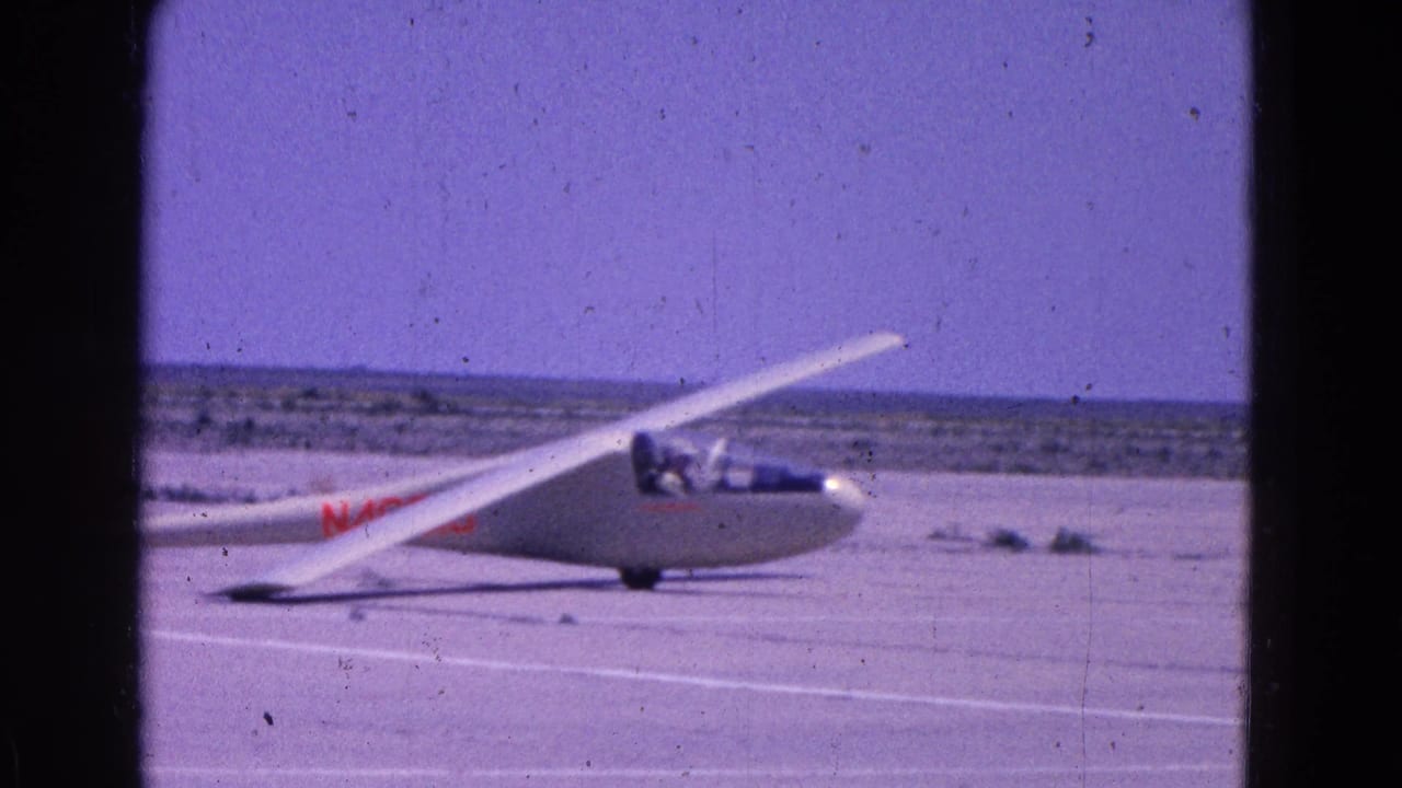 White glider on a runway under a blue sky with dark film borders.