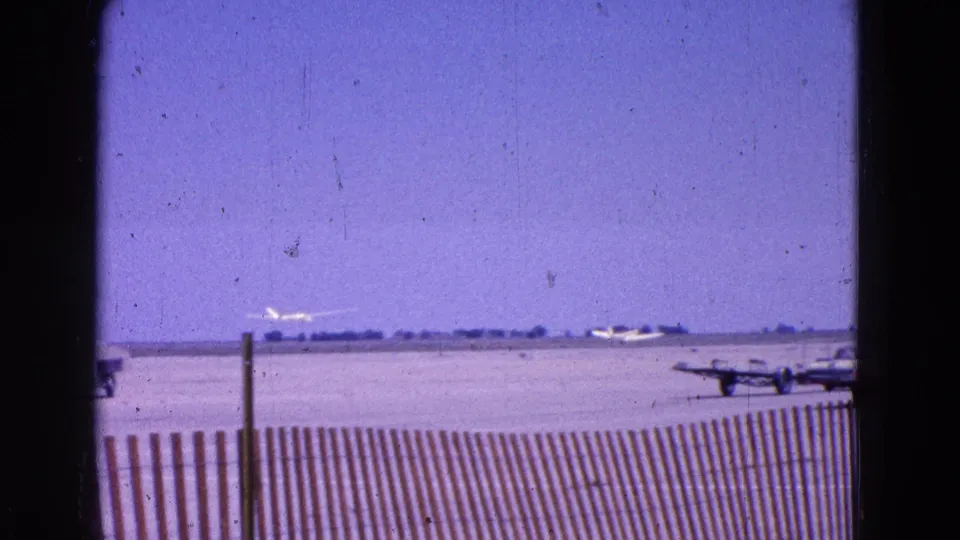 The glider appears farther down the runway in this 1964 airfield view, with fencing and other small aircraft nearby.