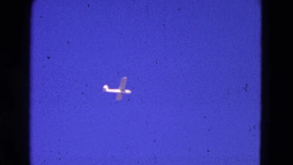 1964 8mm frame from Washington, DC metadata showing a small light airplane against deep blue sky.
