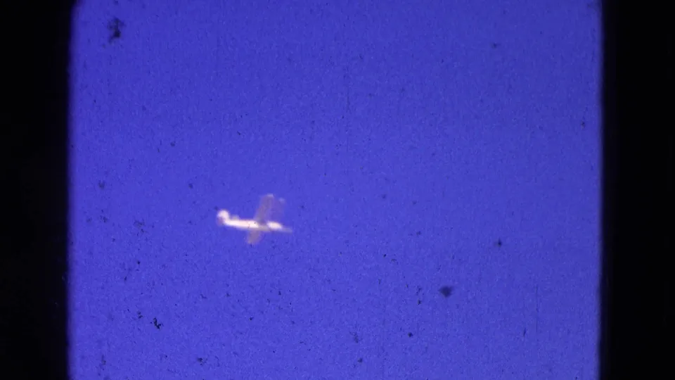Small light airplane continues across the blue sky in 1964 Washington, DC 8mm footage.