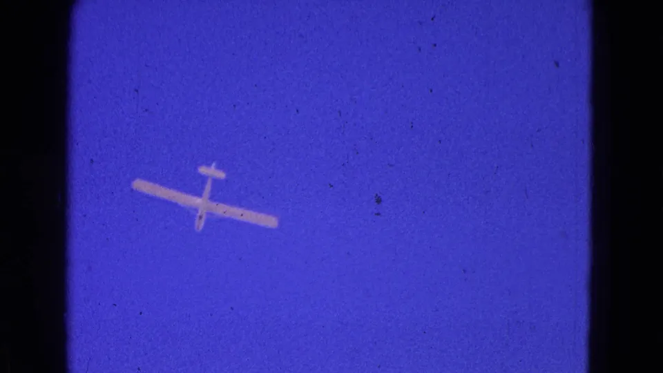 A small airplane is seen from below against blue sky in the 1964 8mm home-movie clip.
