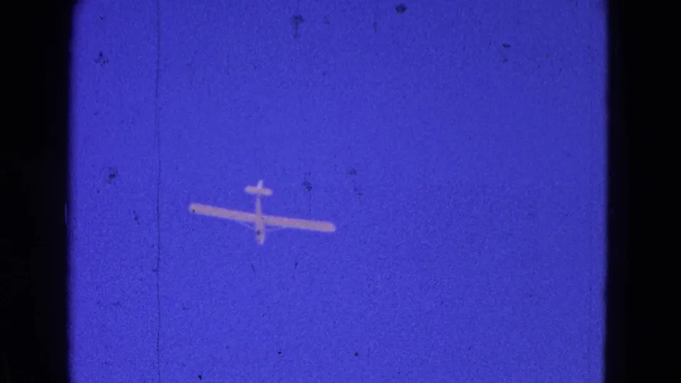 Final frame shows the small airplane from below against blue sky, with visible 8mm grain and scratches.