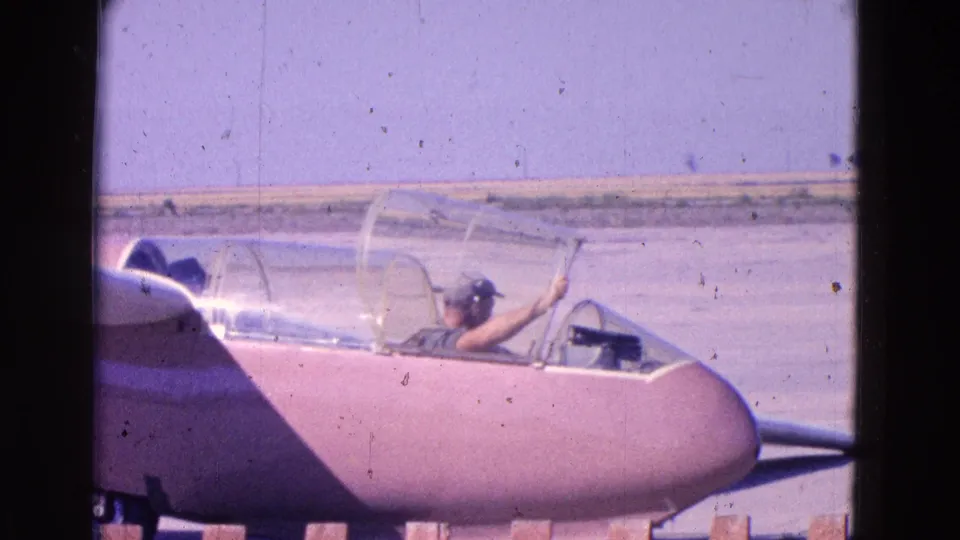 The ground view shows a seated cockpit figure, clear canopy, pinkish glider nose, and airfield tarmac in the Washington, DC area.