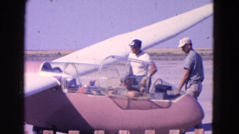 The final frame shows two men beside the pink-and-white glider as the pilot remains seated in the cockpit on the open airfield.