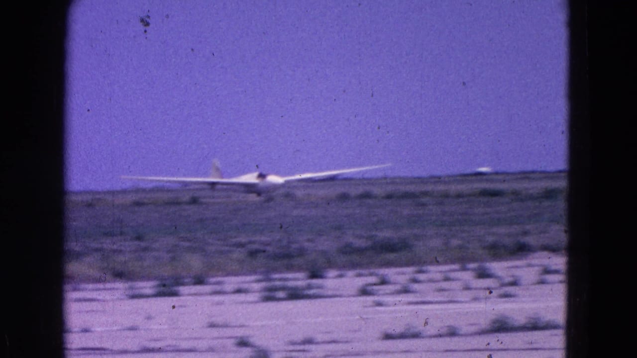 Glider centered near the horizon over a flat, scrubby airfield.