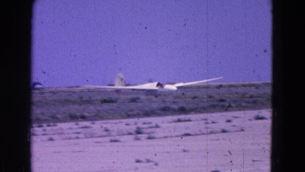 White glider near touchdown on a dusty field beneath a purple sky.