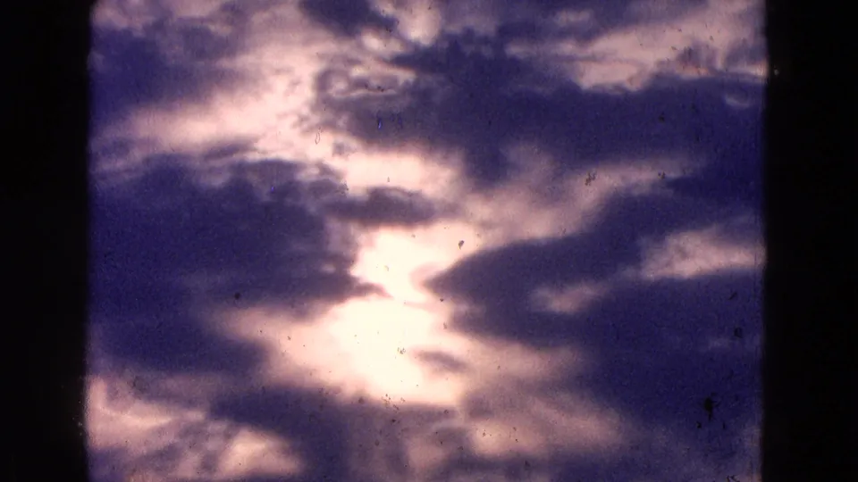 8mm home-movie view of a storm-lit sky, with a bright sun break and soft violet color shift.