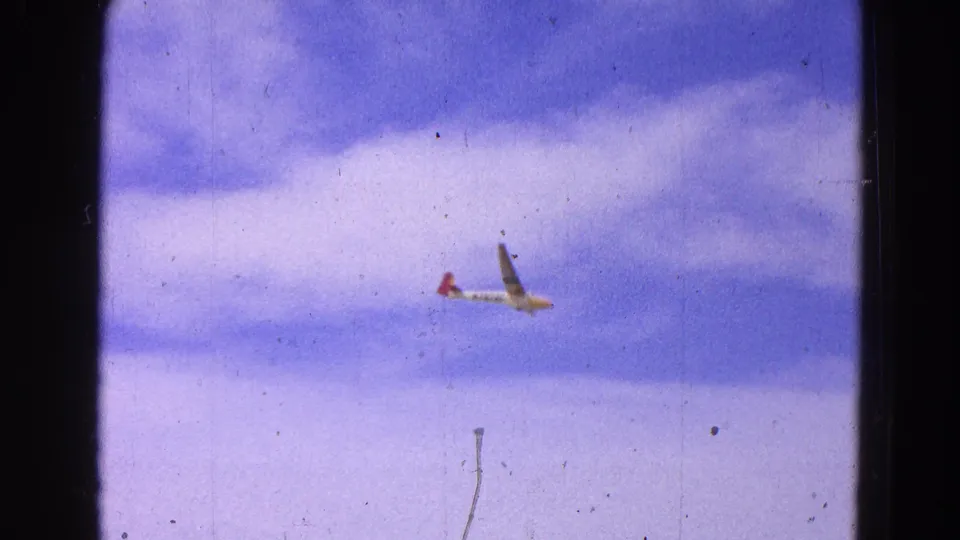 A distant glider with a red tail tip flies across a cloudy sky in 1964 8mm footage from the Washington, DC metadata context.