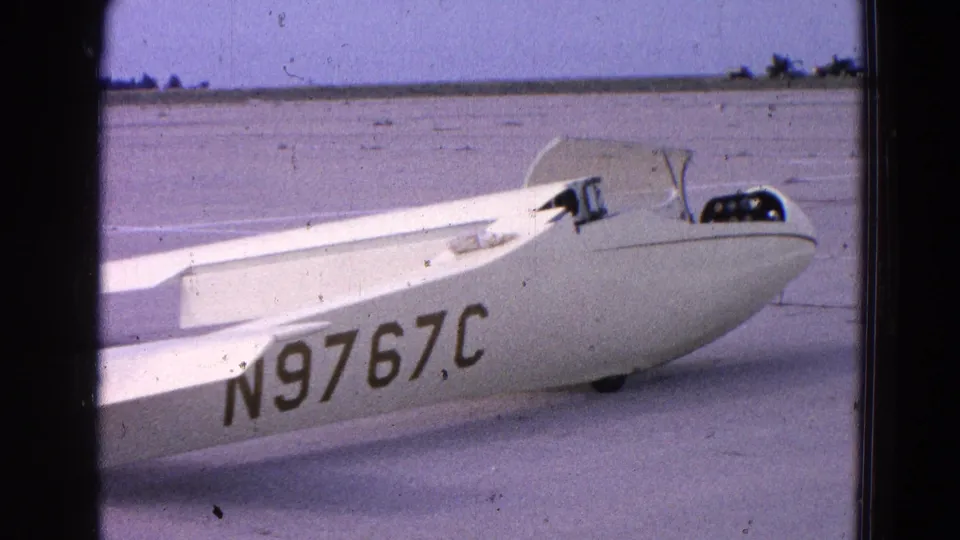 A white glider rests or rolls on a paved airfield, showing cockpit canopy detail and fuselage registration N9767C.