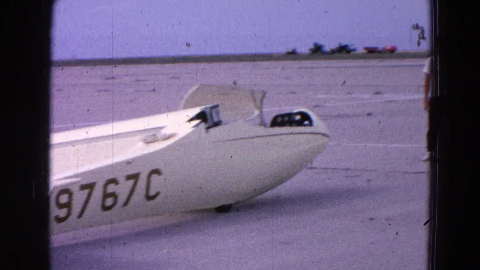 1964 8mm frame showing a white glider fuselage on a Washington-area airfield, with registration N9767C visible on the side.