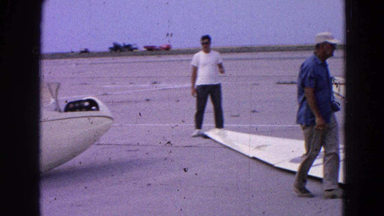 Men stand near a detached glider wing and fuselage on the tarmac.