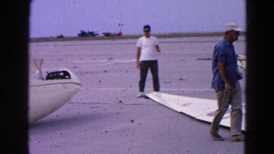 Men stand around a small white glider and detached wing on a 1964 Washington-area airfield, with the aircraft partly assembled.