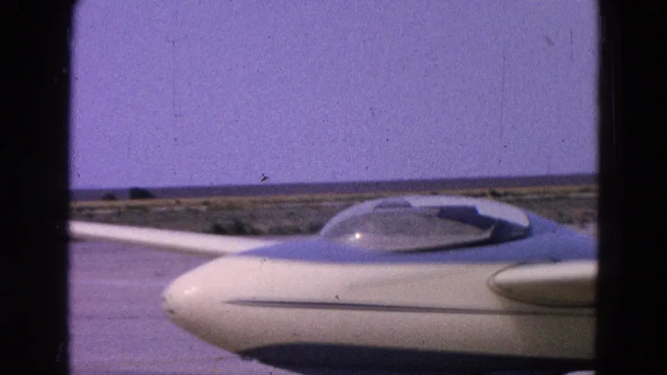 Blue-and-white glider with transparent canopy appears parked on a flat Washington, DC area airfield in 1964 home-movie footage.