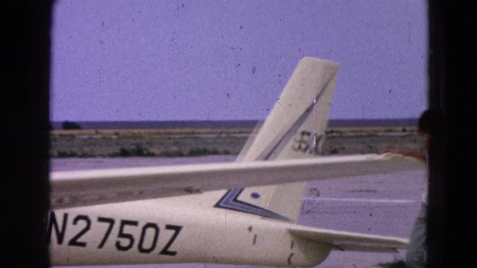 Close 1964 home-movie view of a white glider tail and fuselage marked N2750Z on an open airfield.